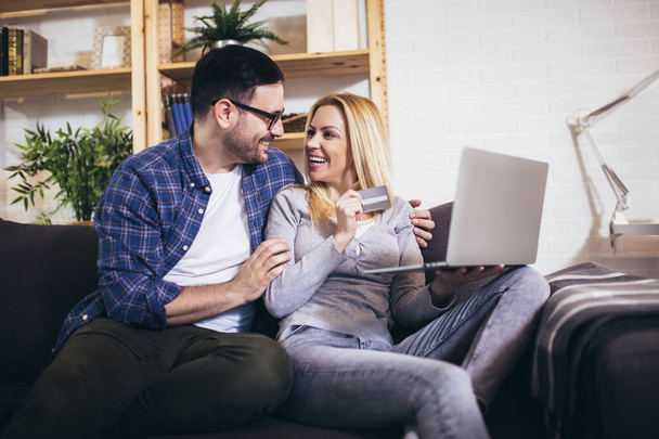 Happy couple communicating while using credit card and laptop for online shopping at home. - Photo, Image