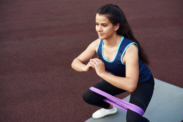Young woman goes in for sports using an elastic band for fitness. A beautiful sportive girl shakes her legs with an expander. - Photo, Image