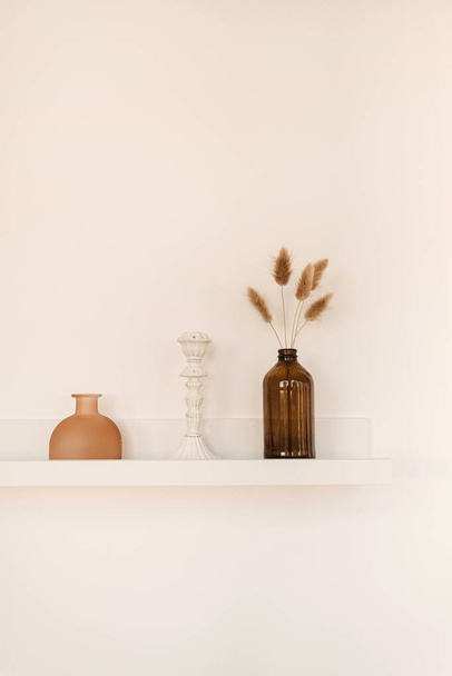 Fehér polc a fehér falon üveggel, vázával, bolyhos pom pom növényekkel, gyertyatartóval. Minimális modern belsőépítészeti koncepció. - Fotó, kép