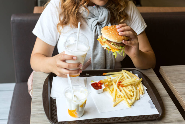 Junk food is comfort food. Girl holds hamburger and milkshake in her hands. Concept: fatty, high-calorie, unhealthy food. Close-up.  - Fotoğraf, Görsel