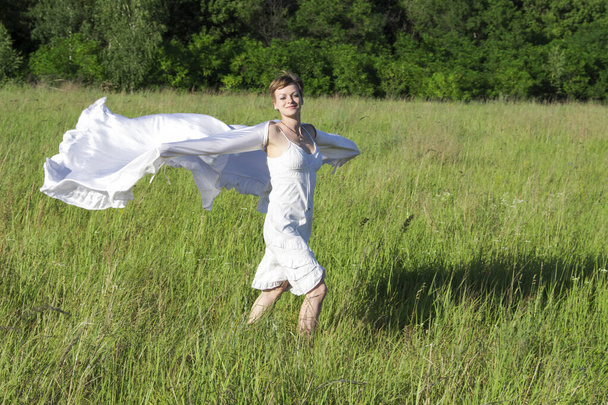 Fille joyeuse dans une robe blanche, court à travers le champ, avec un chiffon blanc sur les mains - Photo, image