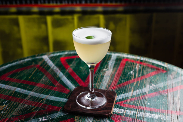 A classic yellow sour cocktail with foam in a nick and nora glass with lime zest garnish - Foto, immagini