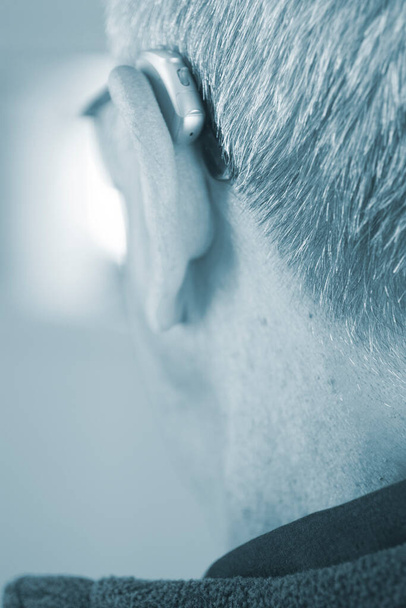 Hombre anciano blanco caucásico que usa audífono digital moderno en la oreja con cabello gris. - Foto, imagen