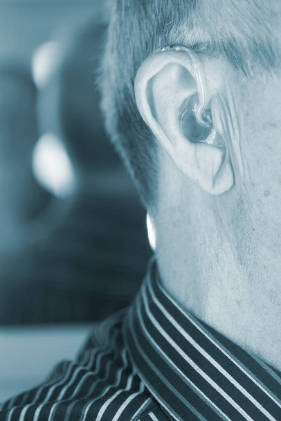 Λευκός Καυκάσιος ηλικιωμένος άνδρας με σύγχρονο ψηφιακό ακουστικό στο αυτί με γκρίζα μαλλιά. - Φωτογραφία, εικόνα