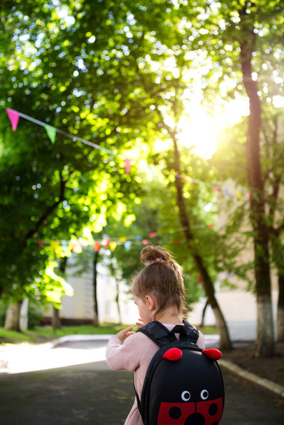 A little girl of Caucasian in a school uniform with a backpack looks at the road in the school yard. Concept back to school. Elementary school, developing activities for preschoolers. Space for text - Valokuva, kuva