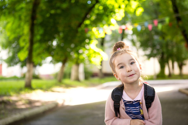 A little girl of Caucasian appearance in a school uniform with a backpack looks into the frame. Concept back to school. Elementary school, developing activities for preschoolers. Space for text - Valokuva, kuva