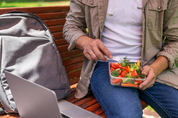 Young man man eating healthy salad outdoors from transparent container - Photo, Image
