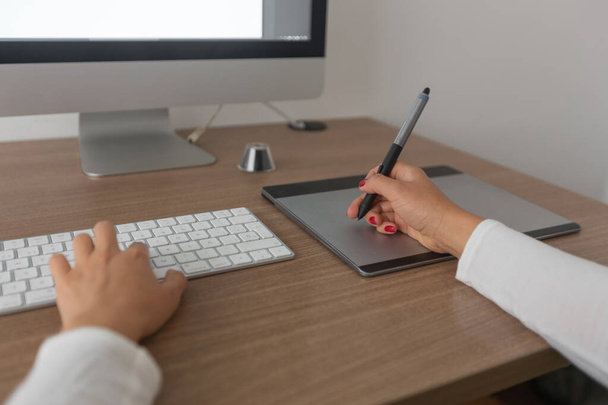 detalle de una vista frontal de una mujer que trabaja en su ordenador dentro de una oficina con un teclado, una tableta digitalizadora, gafas y un escritorio de madera, trabajo - Foto, Imagen
