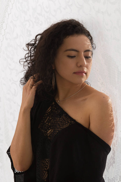 mulher latina com cabelo encaracolado na frente de uma textura de tecido e roupas pretas, mulher mostrando ombro
 - Foto, Imagem