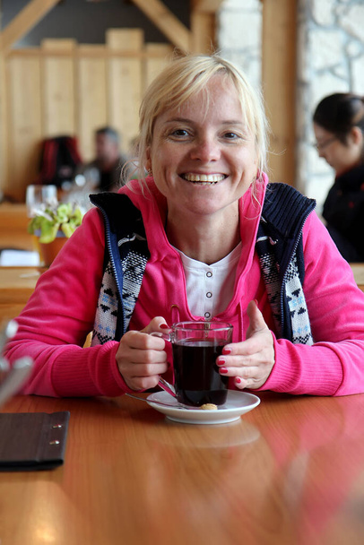 Девушка разогревается с глинтвейном в кафе. Красивая блондинка пьет утренний кофе в помещении. - Фото, изображение