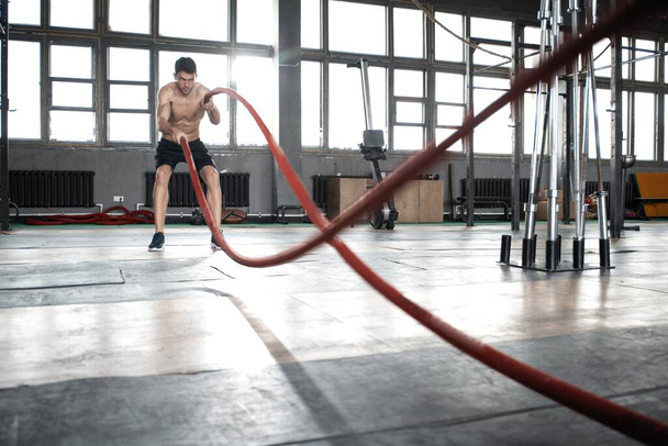 Athletic young man with battle rope doing exercise in functional training fitness gym. - Foto, Imagem