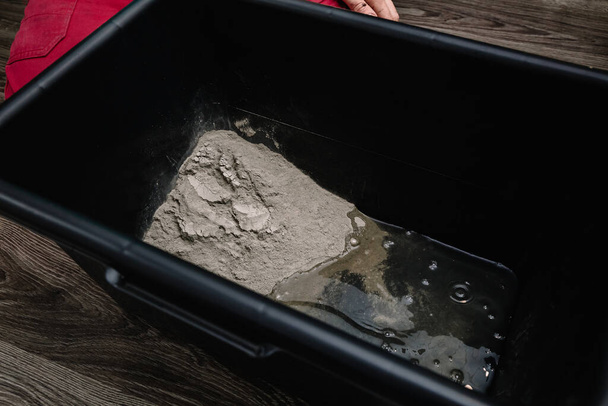 Una persona mescola cemento e acqua in un contenitore per ottenere la miscela finita. Il processo di costruzione, una delle fasi di decorazione. Faccio il gesso. Primo piano. - Foto, immagini