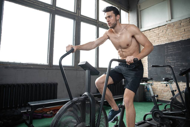 Man using exercise bike at the gym. Fitness male using air bike for cardio workout at Functional training gym - 写真・画像