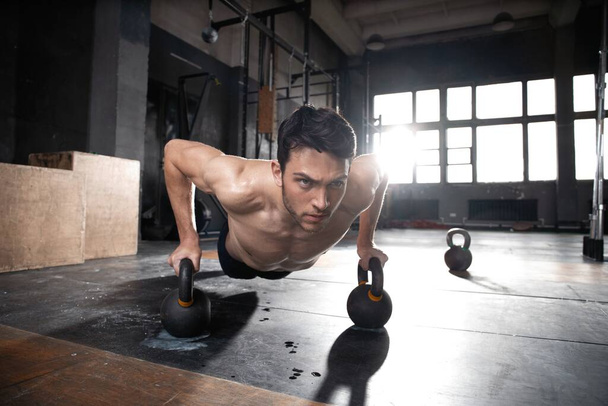 Handsome muscular man doing pushup exercise with dumbbell in a crossfit workout. - Foto, Bild