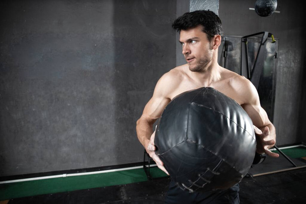 Jeune homme musclé en forme forte faisant lancer le ballon de médecine sur le mur pour l'entraînement Crossfit dur entraînement de base dans la salle de gym - Photo, image