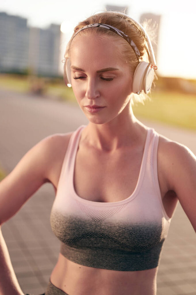 Mujer en forma deportiva agotada en ropa de fitness relajante mientras hace ejercicio físico y escucha música en los auriculares - Foto, imagen