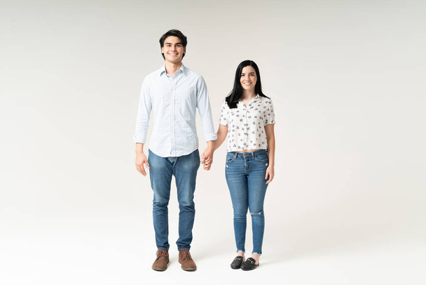 Full length portrait of smiling young couple holding hands against white background - Photo, Image
