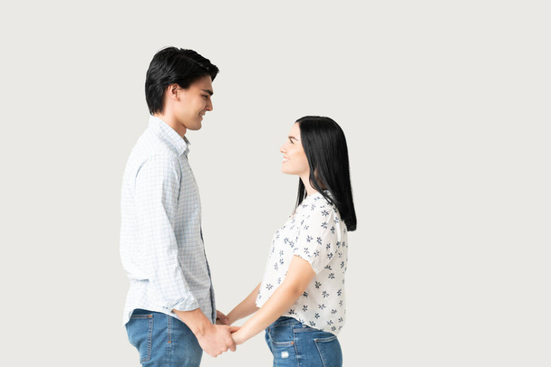 Vista lateral de pareja joven romántica cogida de la mano mientras está de pie cara a cara - Foto, imagen