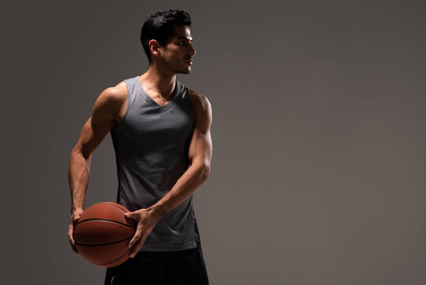 Handsome Hispanic young male athlete with basketball against gray background - Foto, Bild