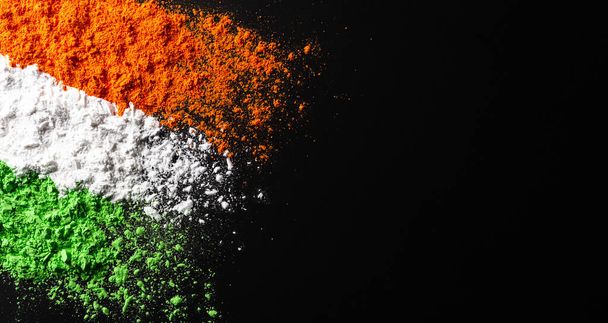 Ινδική Ημέρα Ανεξαρτησίας έννοια υπόβαθρο εορτασμού. Σύμβολα σημαία χρώματα, κόκκινο, πράσινο και πορτοκαλί σκόνη χρώμα πιτσιλισμένο σε σκούρο φόντο. - Φωτογραφία, εικόνα