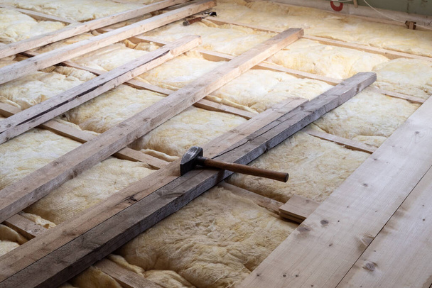 家庭の床の修復のための大工のハンマーと暖かいイソラソンのためのガラスウールの上に木製の板床を敷設 - 写真・画像
