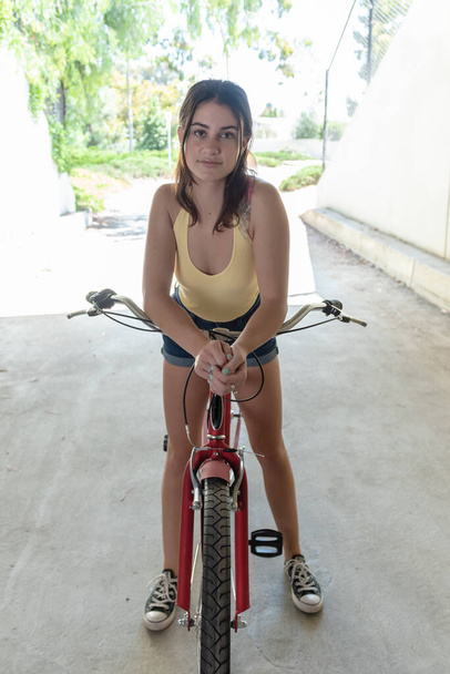 Młodzieńcza nastolatka przechyla głowę w lewo i spoczywa łokcie na kierownicy roweru podczas jazdy w ciepły i słoneczny dzień w południowej Kalifornii. - Zdjęcie, obraz