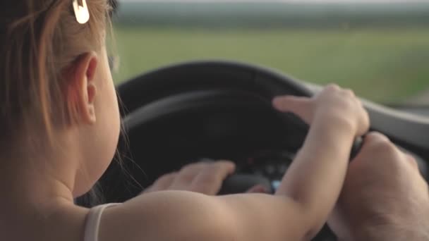 Dad teaches his little daughter to turn steering wheel while sitting in his car in drivers seat. father travels with children by car. driver and kid are driving. happy family and childhood concept - Footage, Video