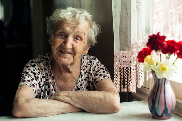 Portret van een oude vrouw gepensioneerde zit aan de keuken in haar huis.  - Foto, afbeelding