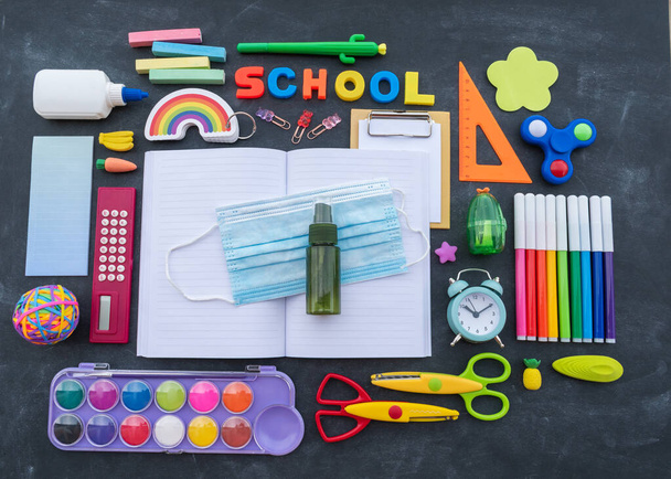 Stationery chalk board. Back to school. Open notepad on top of office supplies. Medical mask and hand sanitizer.Flat lay - Foto, imagen