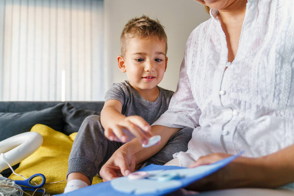 Caucasian woman playing with her son at home - Little boy learning new skills with his mother - Woman and boy learn development games making art craft on the sofa at home - Childhood bonding concept - Foto, imagen