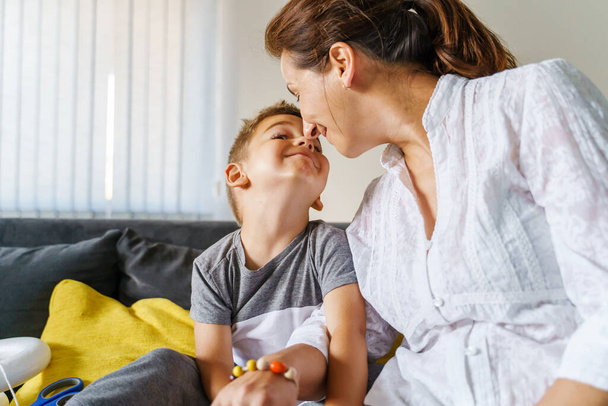 Small boy with his mother at home sitting on the sofa - Mom and son cuddling sharing love - real people childhood domestic life leisure activity happiness and joy support concept - Fotografie, Obrázek