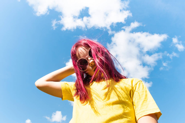 Attractive young girl with pink hair is dancing. Sky background with clouds. Party and fun concept. Kid hair magnificent - Foto, immagini