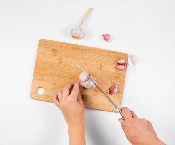 Closeup image of a woman cutting and chopping garlic by knife on wooden board - Foto, immagini