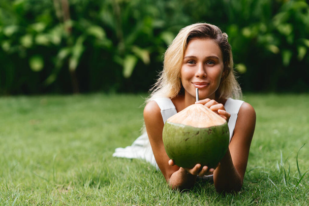 Beautiful blonde woman in the white dress on the tropical terrace with coconut - Fotoğraf, Görsel