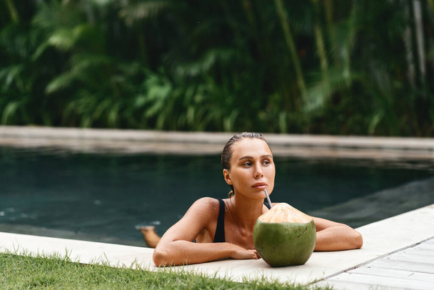 portrait of cute girl with coconut cocktail in the tropical pool. - Foto, Imagem