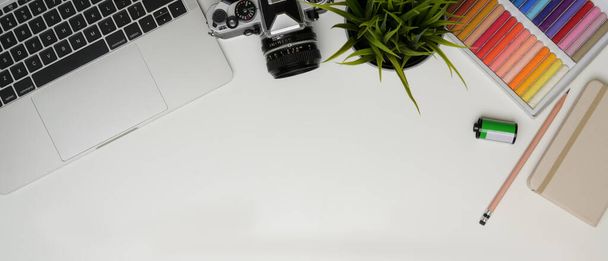 Vista superior do espaço de trabalho com laptop, câmera, ferramentas de pintura, papelaria e espaço de cópia na mesa branca
  - Foto, Imagem