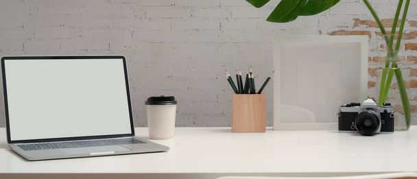Close-up zicht op moderne werkruimte met mock up laptop, briefpapier, camera, decoraties en kopieerruimte op wit bureau - Foto, afbeelding