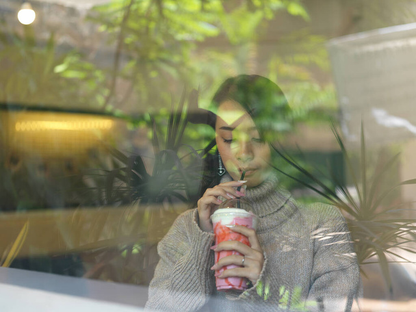 カフェのカウンターバーに座っている間、肖像画は若い女性の飲酒スムージーの窓を貫通ショット - 写真・画像