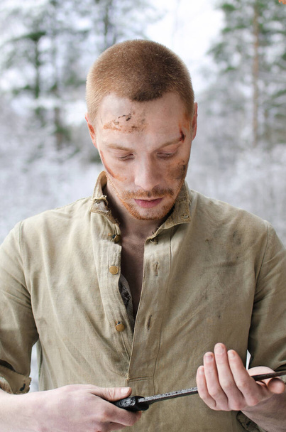 νεαρός άνδρας σε μια στρατιωτική στολή του Β 'Παγκοσμίου Πολέμου με ένα μαχητικό σπαθί στα χέρια του σε ένα χιονισμένο δάσος του χειμώνα - Φωτογραφία, εικόνα