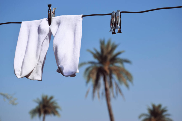 Bílé ponožky visely na drátu, modrá obloha a palma v pozadí - Fotografie, Obrázek
