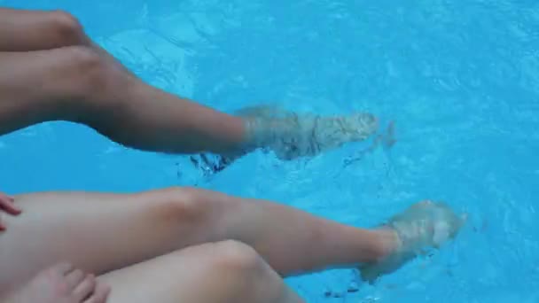 Two barefoot tanning young model sitting poolside joy sunlight testing blue water kicking shaking foot in public pool make beautiful splashes big waves in rest exotic trip tourist resort, closeup view - Video