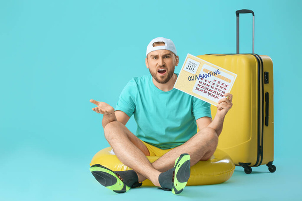 Hombre enojado sosteniendo el calendario con la palabra escrita QUARANTINE contra el fondo de color. Concepto de vacaciones - Foto, Imagen