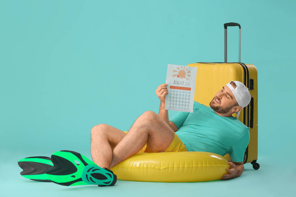 Young man with calendar and suitcase on color background. Vacation concept - Фото, зображення
