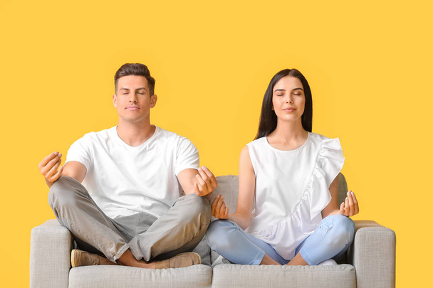 Young couple meditating on sofa against color background - Foto, Imagem
