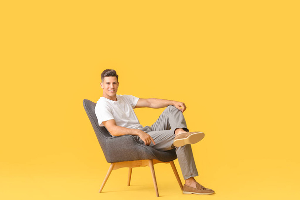 Молодий чоловік розслабляється в кріслі на кольоровому фоні
 - Фото, зображення