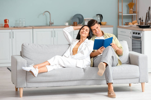Jovem casal com livro relaxante no sofá em casa
 - Foto, Imagem