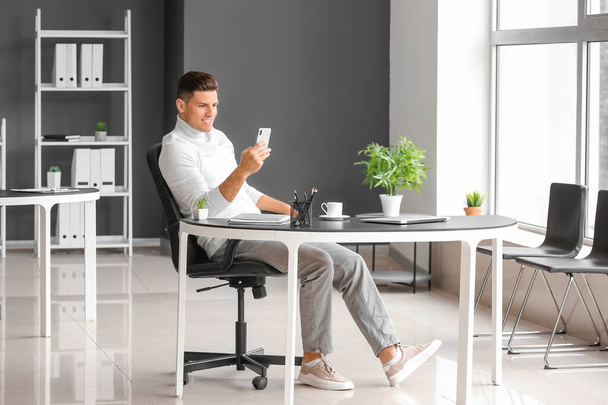 Junger Mann mit Handy entspannt sich am Arbeitsplatz im Büro - Foto, Bild
