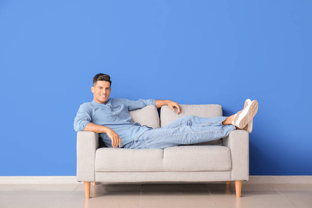 Young man relaxing on sofa near color wall - 写真・画像