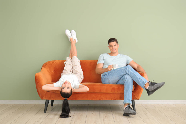 Молодая пара отдыхает на диване рядом с цветной стеной - Фото, изображение