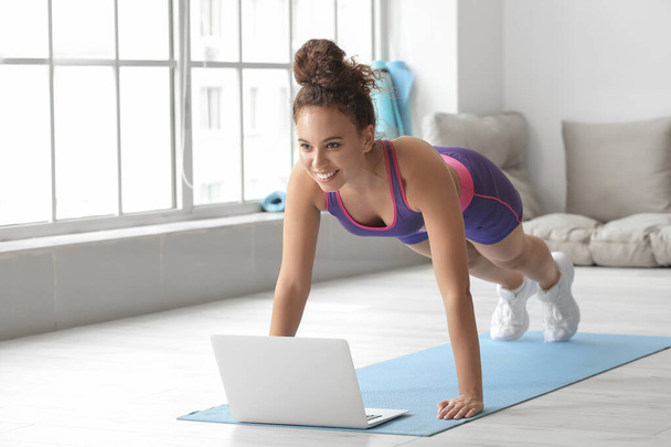 Sporty young woman with laptop training at home - Fotó, kép